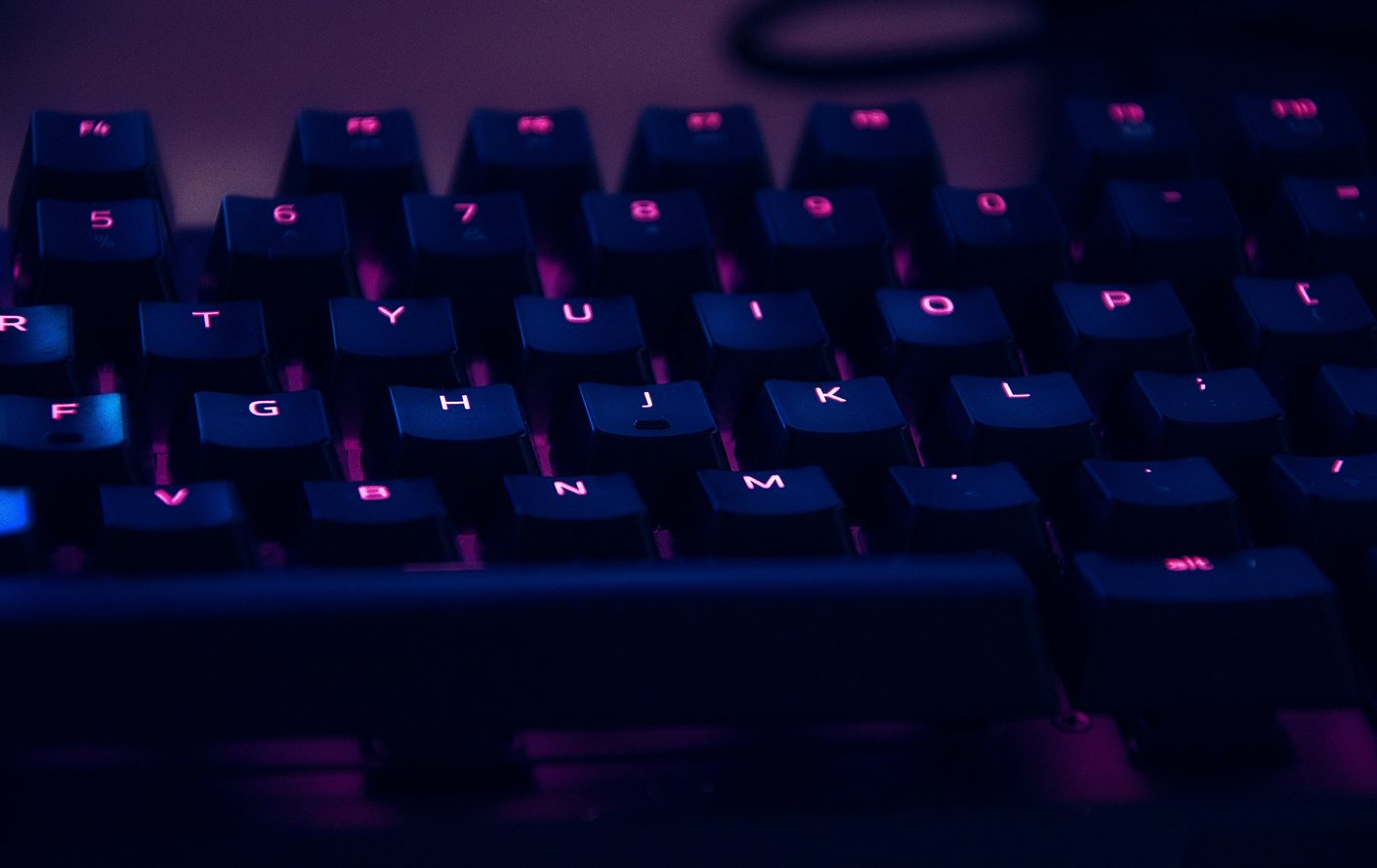 A backlit mechanical keyboard glowing pink and blue in a darkened room