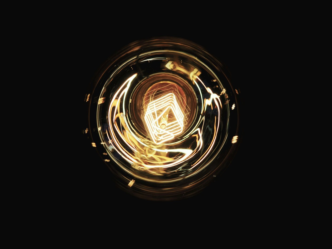 The glowing coiled filament of an incandescent bulb photographed against a black background