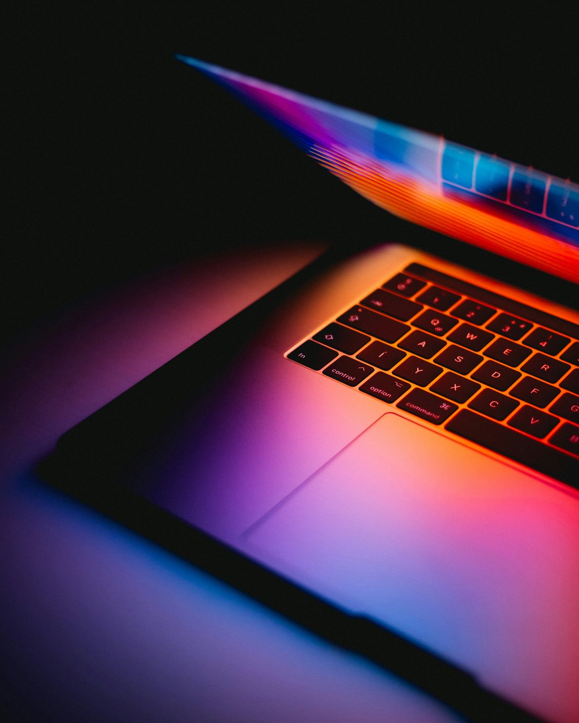 A laptop half open in darkness, its keyboard washed in orange and blue light