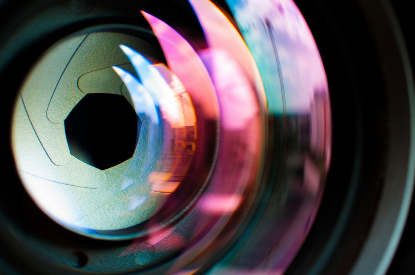Extreme close-up of a camera lens aperture with coloured light refracting across the glass
