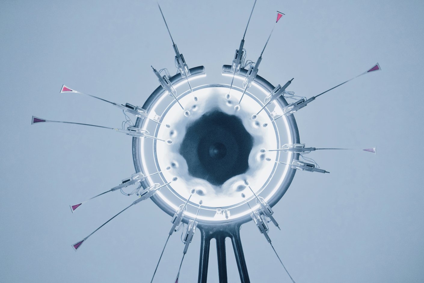 A ring-shaped lamp with slender instruments radiating outward against a pale sky