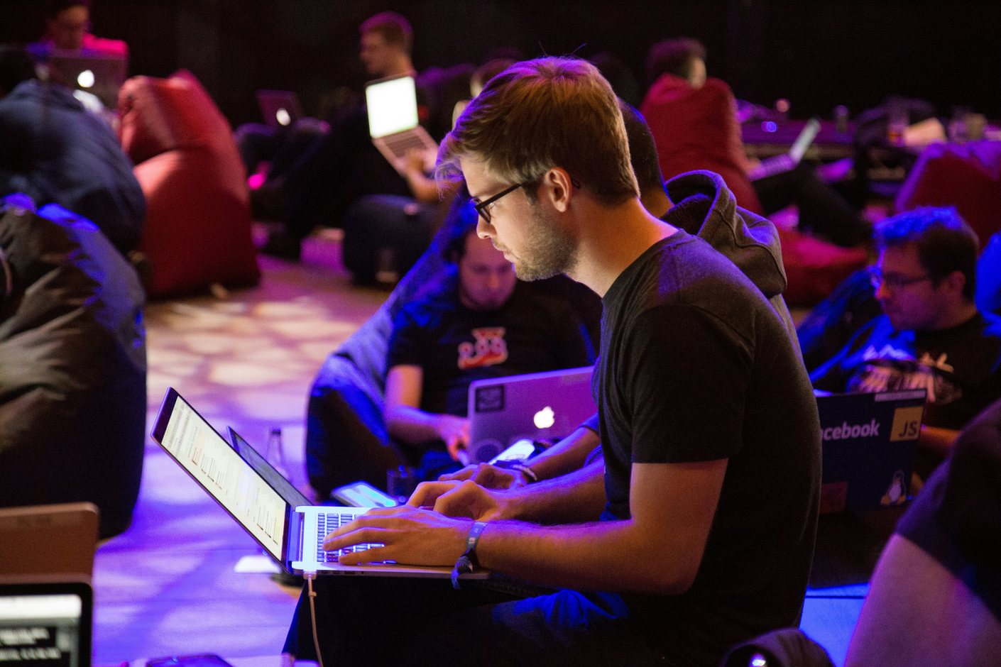 A person working intently on a laptop among others in a dimly lit late-night work session