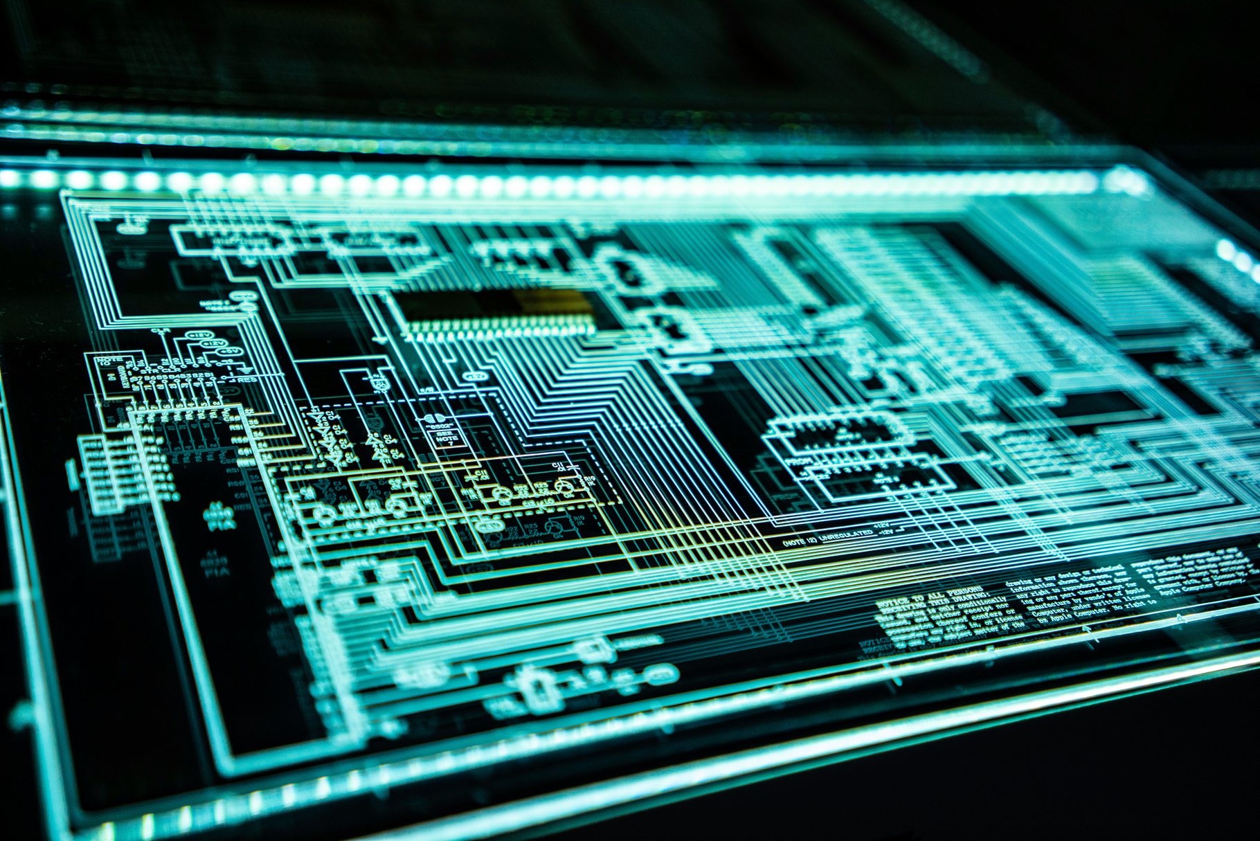 A backlit technical circuit drawing glowing on a light table in a darkened room