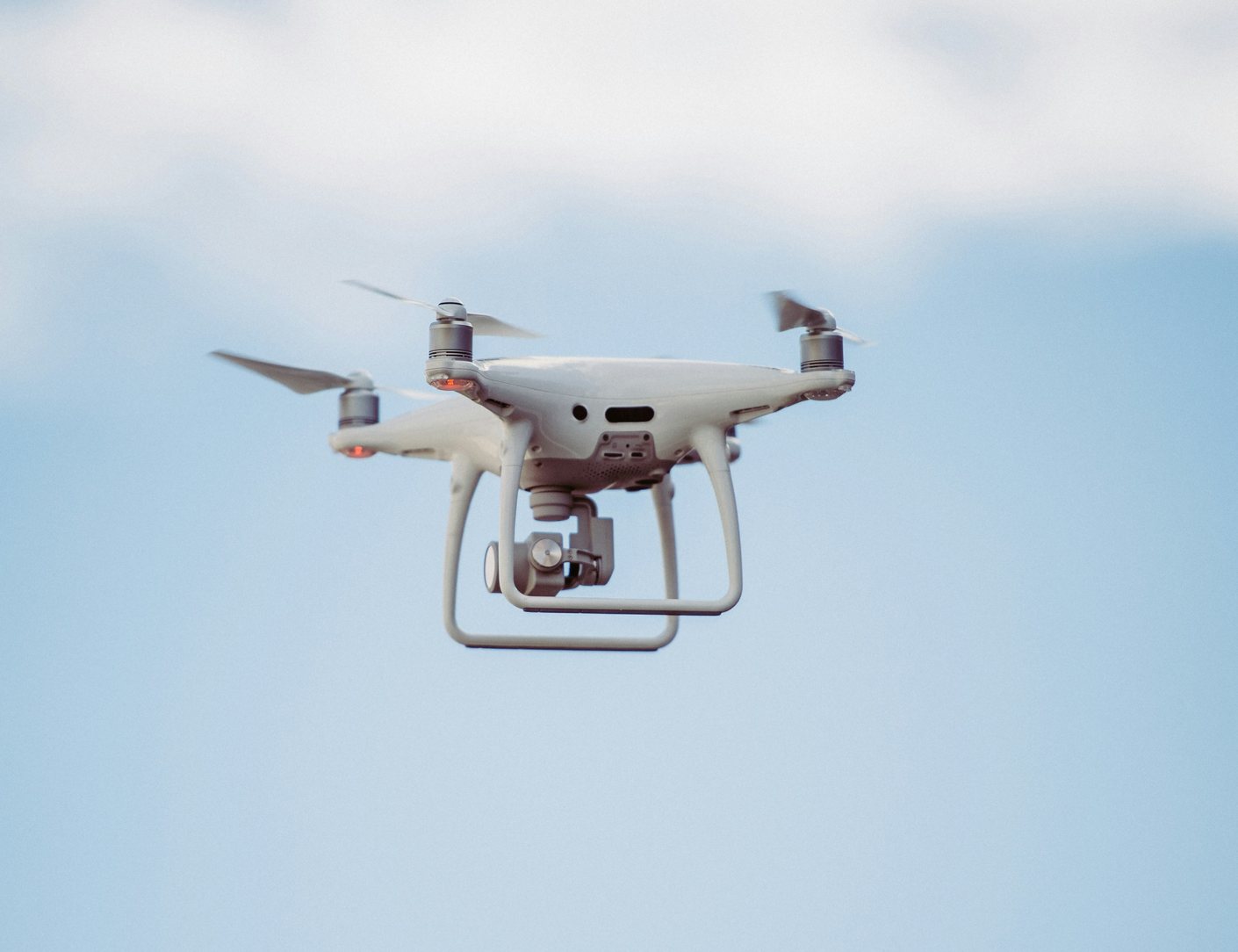 A white four-rotor drone hovering against a pale overcast sky