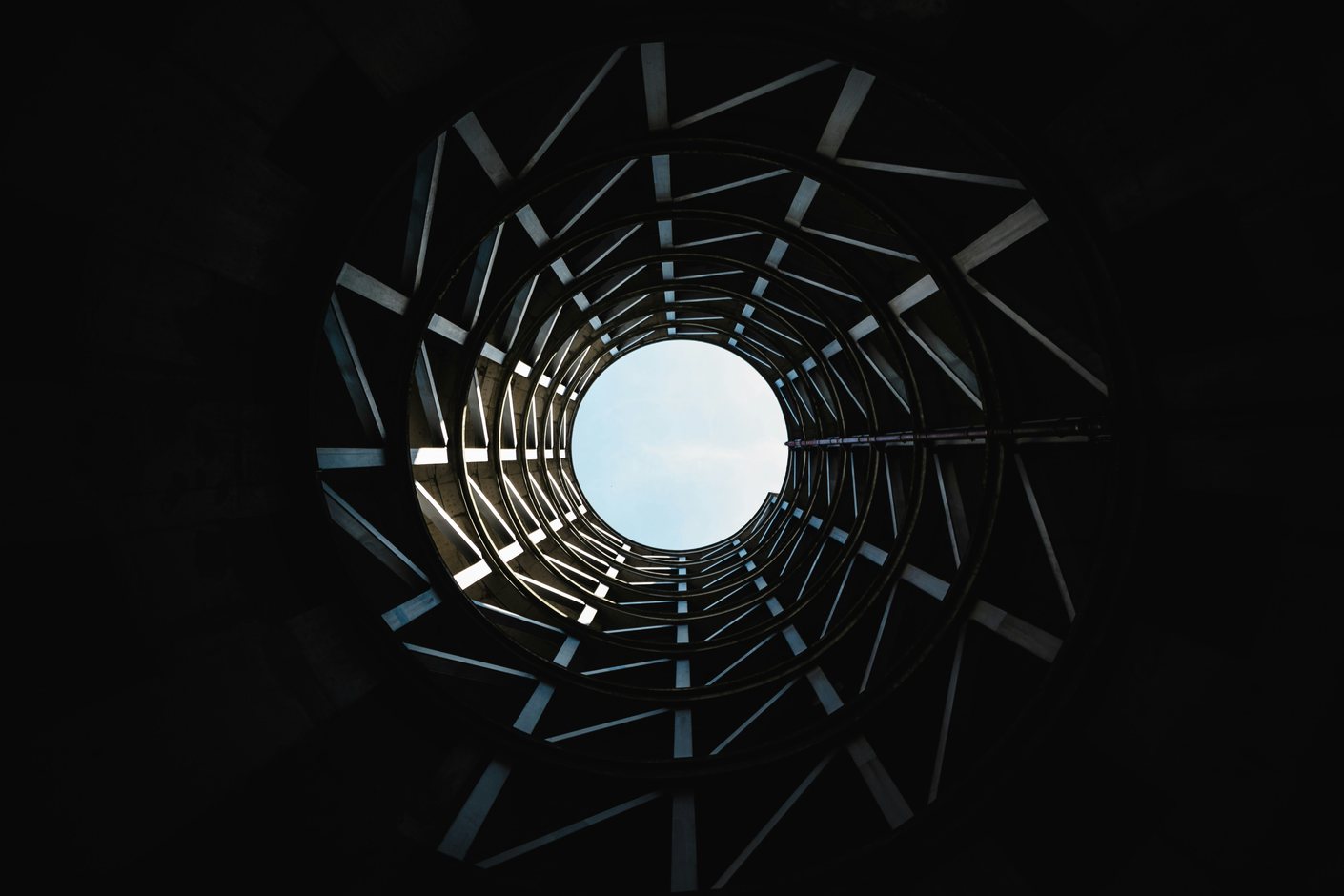 A spiral staircase seen from directly below, coiling upward to a circle of open sky